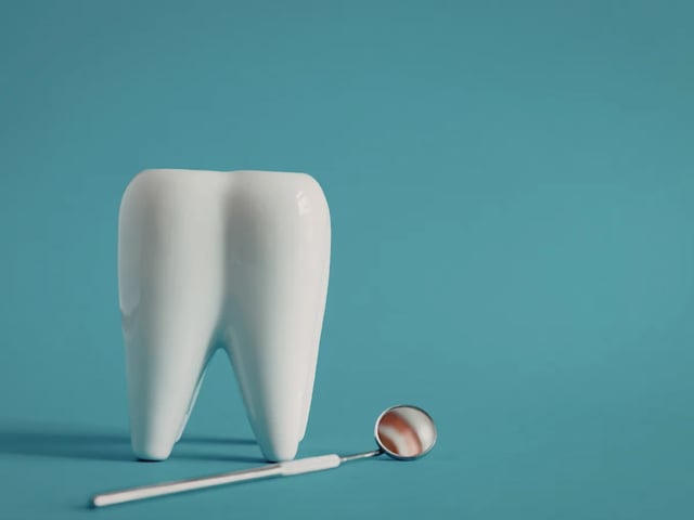 Emergency Dentist on Avenue Road | Broken Tooth Repair at North Toronto Dental Centre White ceramic tooth model and dental mirror on a teal background representing emergency broken tooth repair
