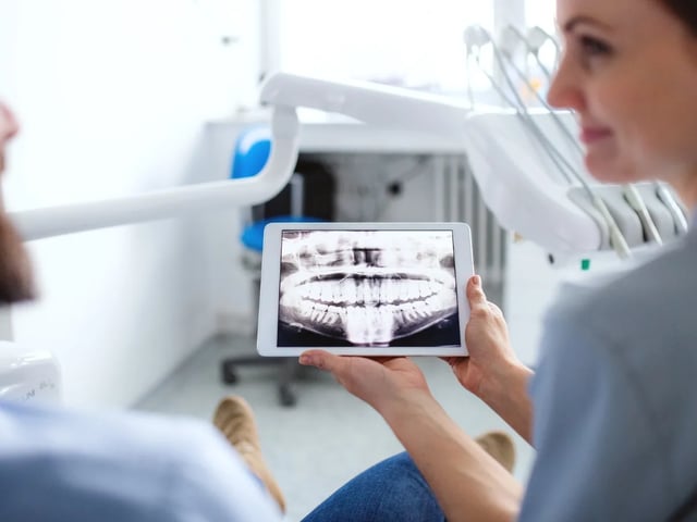 Dentist on Avenue Rd: What Your X-Rays Reveal | North Toronto Dental Centre Dentist reviewing a digital panoramic X-ray with a patient on a tablet in a modern dental office
